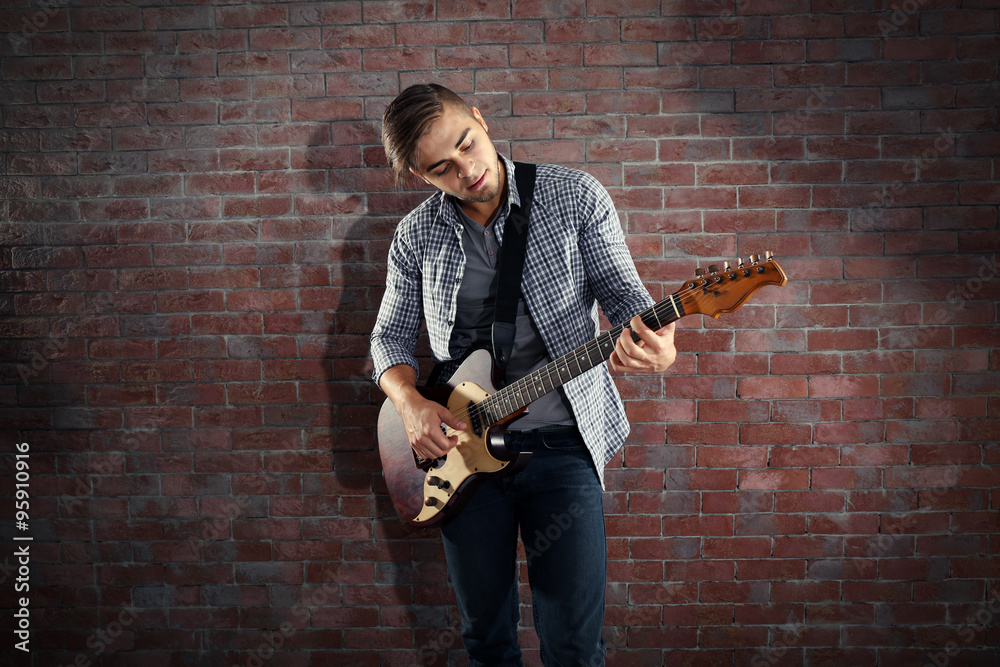 Young man playing guitar on brick wall background