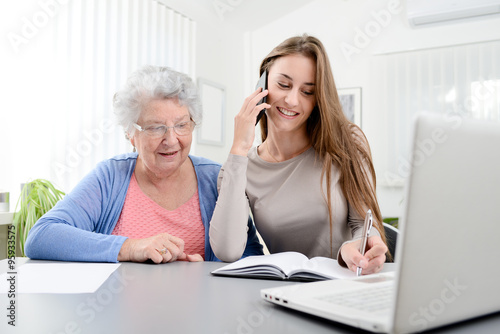 Fotografie, Obraz young woman helping an old senior woman doing paperwork and administrative proce