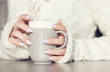 © NinaMalyna - Close up of woman's hands holding cup of hot coffee drink. She is wearing warm cardigan. Winter chill out and lifestyle concept.