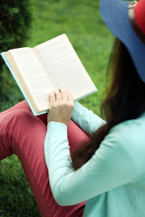 Wall Mural - Young woman with book sitting on green grass outdoors