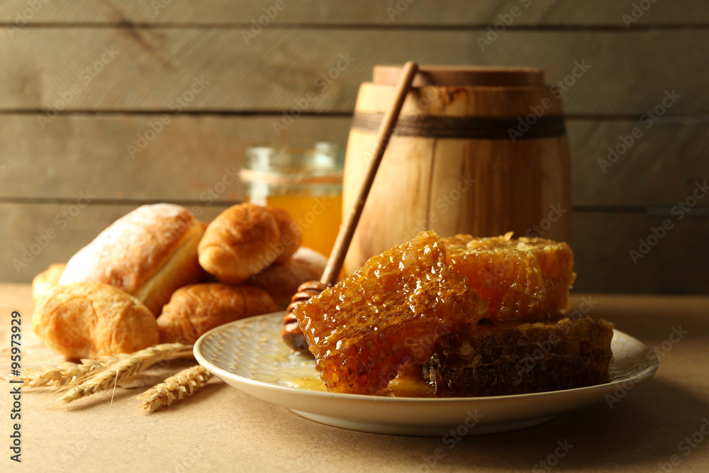 Honeycombs on plate, hot buns in basket on wooden background