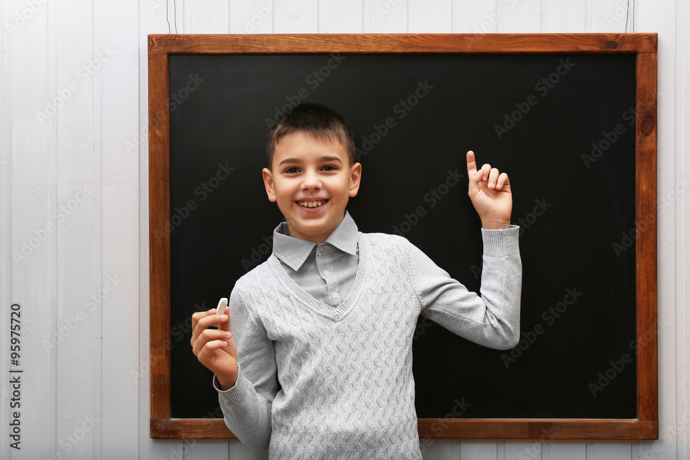 Young cute schoolboy standing at the blackboard