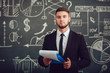 © kanashkin - A bearded man in a suit standing with a folder near whiteboard with graphs