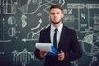 © kanashkin - A bearded man in a suit standing with a folder near whiteboard with graphs