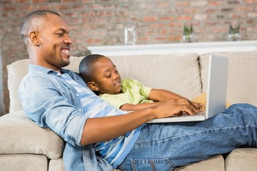 Wall Mural - Father and son using laptop on the couch