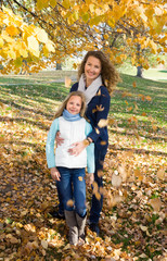 Mother and daughter standing under falling yellow leaves