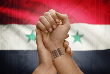 Barcode ID number on wrist of dark skinned person and national flag on background - Syria