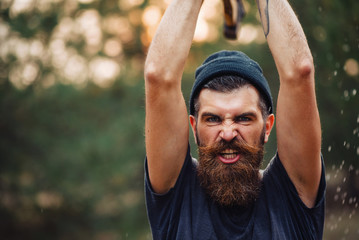 Wall Mural - Brutal brunette bearded man in warm hat with a hatchet in the woods on a background of trees