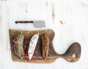 Wall Mural - French alsacian smoked salamis on rustic walnut wooden chopping board over white backdrop, top view