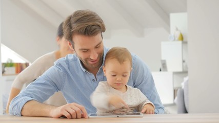 Wall Mural - Parents watching baby girl play with digital tablet