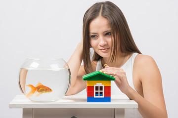 Wall Mural - The girl looks at a goldfish and put her hand on the toy house