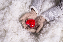 Woman Hands In Light Teal Knitted Gloves Are Holding Beautiful Entwined Vintage Red Heart In A Snow. St. Valentine Concept.