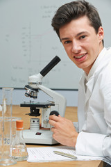 portrait of male pupil using microscope in science laboratory