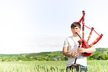 Picture Of Young Man Playing Pipes In National Uniform On Green Summer Outdoors Copy Space Background