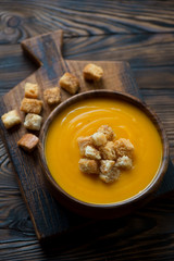 Wall Mural - Pumpkin cream-soup with croutons in a wooden bowl, studio shot