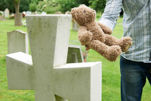 Father Placing Teddy Bear On Child's Grave In Cemetery