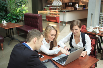 Wall Mural - Businessmen sitting in cafe for a laptop, discussing plans. two girls and man