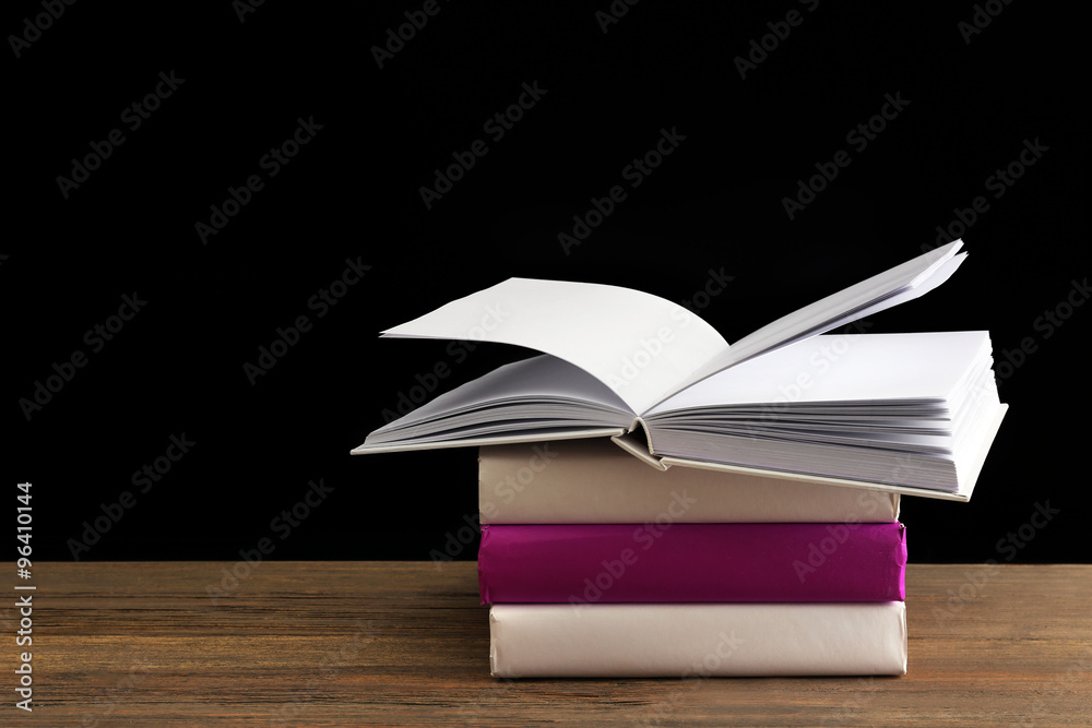Pile of different books on wooden table against black background