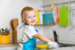 Toddler child washing dishes in kitchen. Little boy having fun with helping to his mother with housework