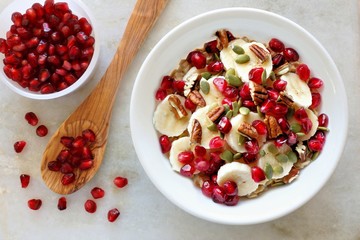 Wall Mural - healthy breakfast oatmeal with pomegranate, bananas, seeds and nuts, overhead scene on white marble