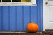 An orange pumpkin on the front porch of a purple house.