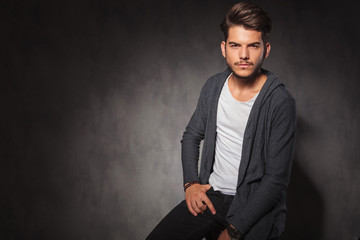 man posing in studio with hand in pocket while sitting