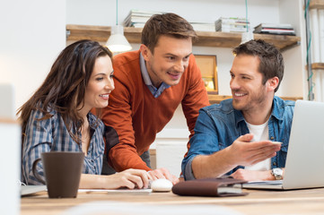 Happy colleagues working together at laptop