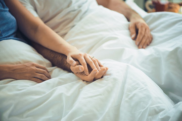 Wall Mural - Young man and woman in bed, holding hands