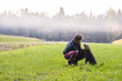 Young man crouching to pet his black dog in a beautiful green me