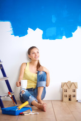 Wall Mural - Portrait of female painter sitting on floor near wall after paintingand holding a cup