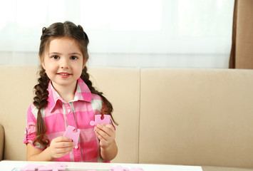 Cute little girl playing with puzzles on home interior background