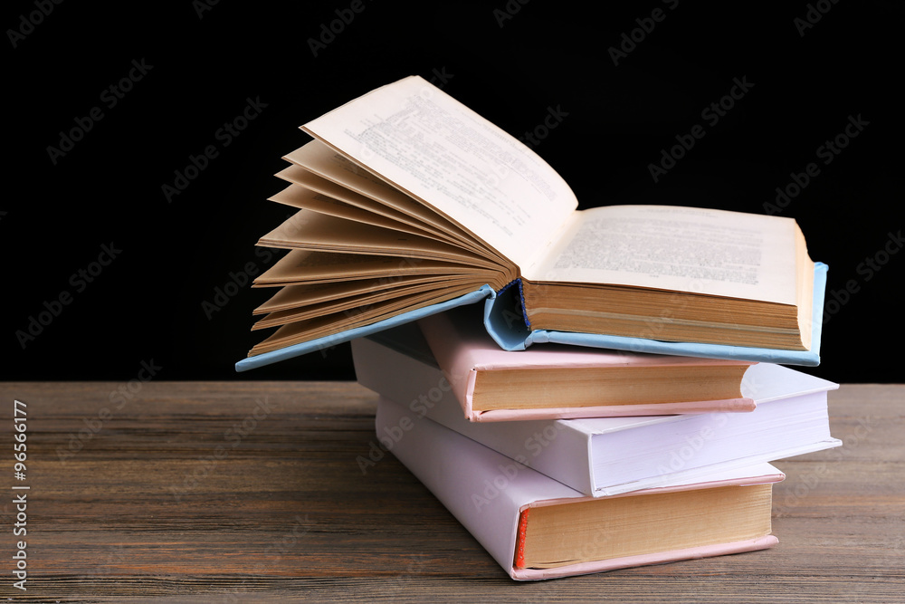 Pile of different books on wooden table against black background
