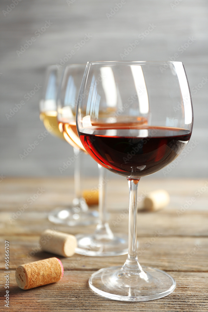 Wine glasses in a row and corks on wooden table against grey background
