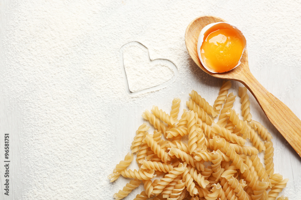 Heart of flour and pasta on gray background