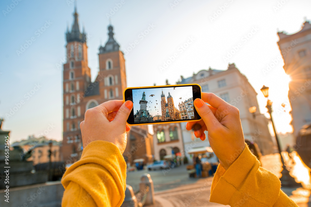 Obraz Female hands photographing with mobile phone old city center in Krakow fototapeta, plakat
