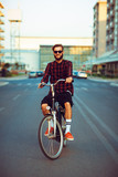 Fototapeta Miasto - Man in sunglasses riding a bike on city street