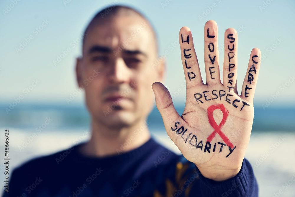 young man with a red ribbon for the fight against AIDS in his ha - obrazy, fototapety, plakaty 