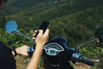 Young man sitting on scooter and using smartphone on green backg