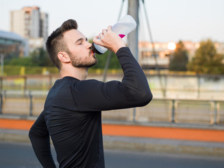 Wall Mural - Young handsome runner with water bottle sitting on a bridge