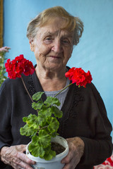 Wall Mural - An elderly woman stands on the balcony with homemade flowers in hand.