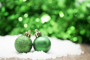 green christmas balls on snow against green bokeh background