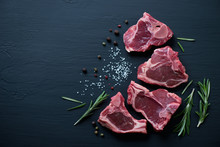 Raw T-bone Lamb Steaks With Seasonings On A Black Wooden Surface