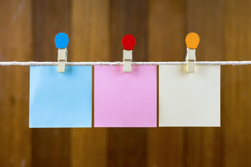 Wall Mural - Blank colorful sticky papers hanging by a rope against blurred wooden background.