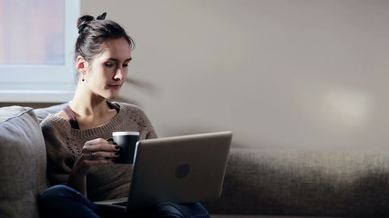 Woman sitting in sofa and working on laptop