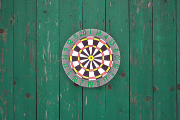 Front view of round target for darts hanging on old wooden fence painted green color