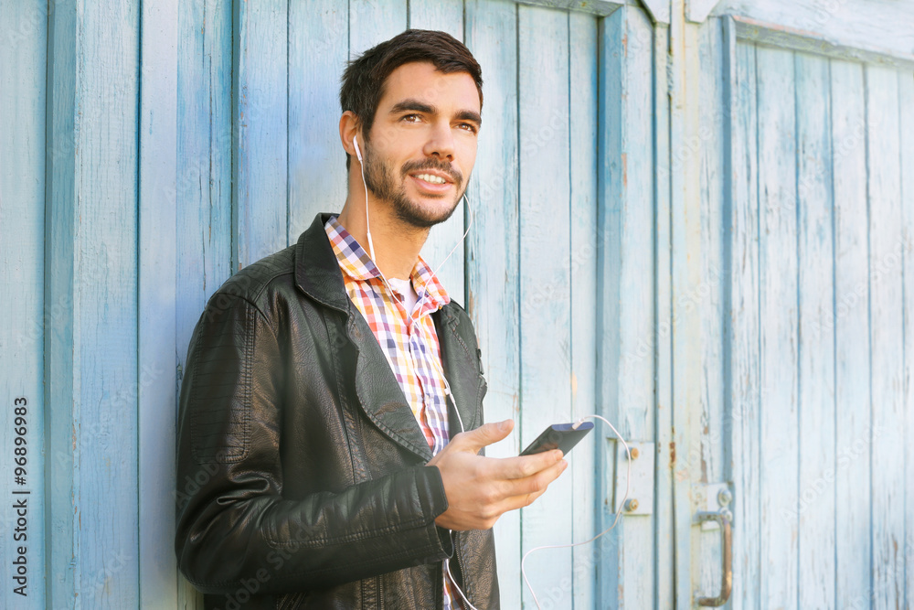 Young man listening to music on a house wall background
