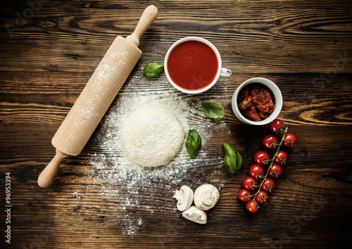 Cuadros en Lienzo Masa de pizza con los ingredientes en la madera