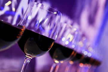 Wall Mural - Nightclub wine glasses with red wine lit by party festive lights on dark-purple background, nightlife 