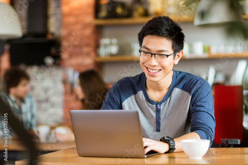 Foto Happy cheerful asian male smiling and using laptop in cafe