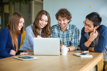 Wall Mural - Group of positive cheerful students doing homework together in classroom